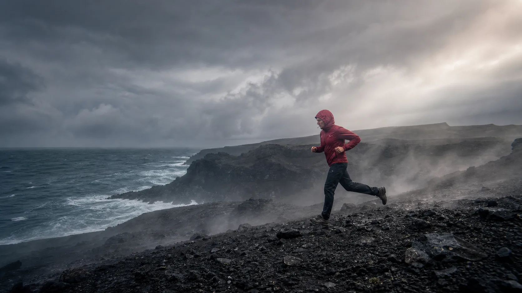Trail runner crossing a stormy volcanic coastline